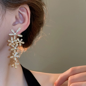 Close-up of gold tassel earrings featuring sparkling zircon flowers on a female model