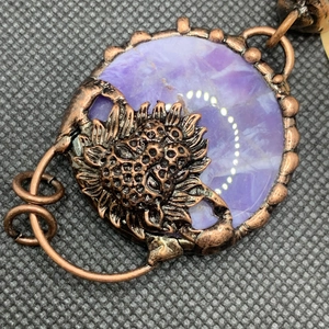 Detail of vintage copper pendant featuring a purple gemstone and sunflower motif