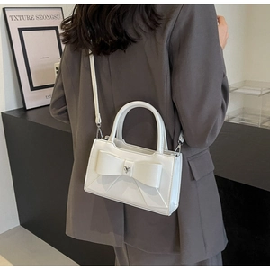 Close-up of a white leather bow square bag worn over a grey blazer with heart detail