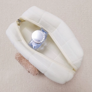 Top view of open white quilted makeup bag with soft fabric and brown plush charm