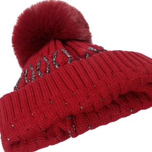 Dark red chunky knit beanie with gold thread accents and large faux fur pompom detail