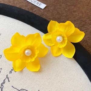 Gros plan détaillé sur des boucles d'oreilles fleur en tissu jaune avec une perle au centre