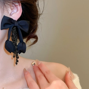 Detail of black fabric bow earring with crystal tassels worn on a female model