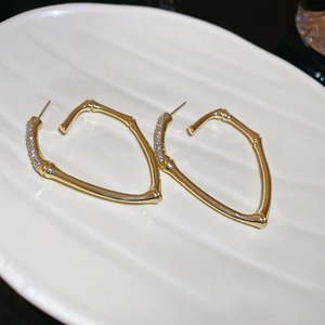 Detail shot of golden bamboo-shaped earrings with rhinestones on a white tray