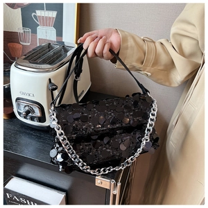 Detail of elegant black sequin handbag featuring chunky silver chain and leather strap