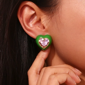 Gros plan d'une boucle d'oreille cœur plaquée or 18K avec émail vert et zircon violet
