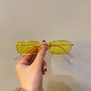 Detail of narrow rectangular yellow sunglasses with slim gold metal frame in hand