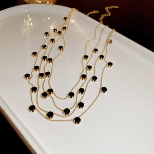 Detailed view of multilayer gold necklace with black round beads on a ceramic tray