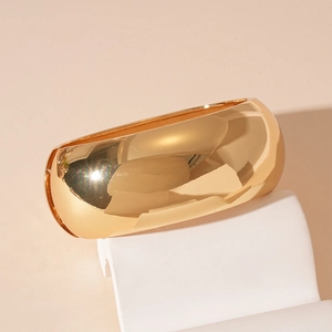 Detailed close-up of wide irregular gold metal bangle on a modern geometric display stand