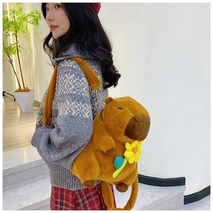 Capybara plush backpack with yellow flower detail worn by a model in a cozy indoor setting