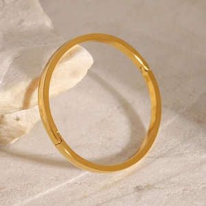 Poliertes goldener Edelstahl-Armreif mit Verschluss auf naturfarbenem Stein