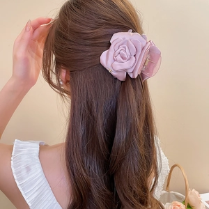 Vista posteriore di una molletta con rosa in raso rosa su lunghi capelli castani