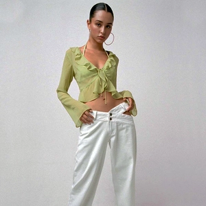 Detail of light green sheer ruffled long sleeve top with tie-up V-neck and white pants