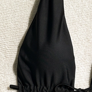Close-up of black halter one-piece swimsuit featuring ruched fabric and tie-front details