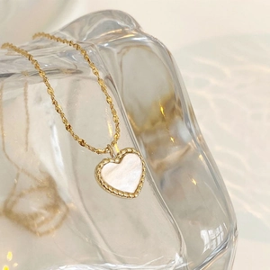 Elegant gold heart pendant necklace with white shell inlay on artistic glass display