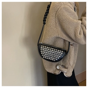 Detail of black crescent crossbody bag featuring silver rivets and woven leather strap
