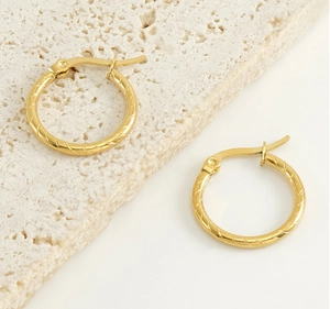 Detail of gold twisted hoop earrings on beige stone showing refined texture and luster