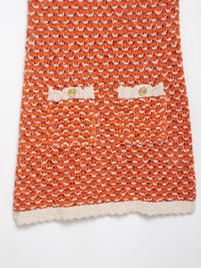 Detail of orange and white textured knit dress featuring a gold embossed decorative button