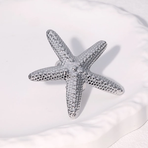 Polished silver starfish ring with textured surface on a white embossed ceramic plate