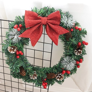 Close-up of artificial pine wreath featuring a large red glitter bow and natural pine cones