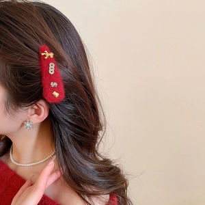 Close-up of red plush hair clip with golden bow and pearl necklace for New Year styling