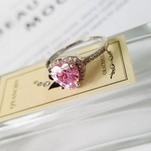 Macro detail of a silver heart ring featuring a pink gemstone and diamond-paved band