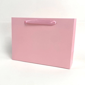 Minimalist pink paper gift bag with satin ribbon handles shown at a 45-degree angle