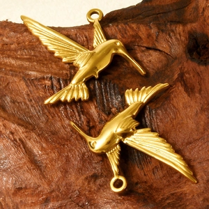 Two golden stainless steel bird pendants in flight pose on a rustic wood background