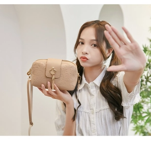 Detail of beige camera bag featuring cartoon embossing and a gold crown metal buckle