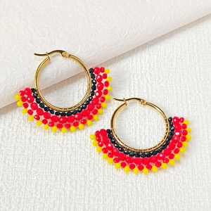 Detail of handmade beaded hoop earrings with black red and yellow seed beads on gold ring