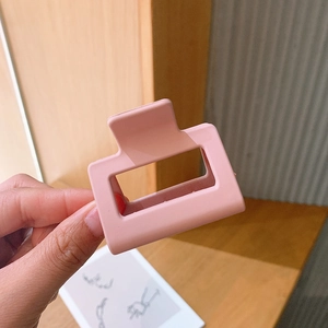 Detail of a small matte pink rectangular claw clip held by hand for scale