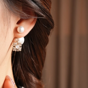 Close-up of pearl and gold flower stud earring with zircon on model's ear