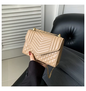 Detail of beige quilted shoulder bag with gold chain strap and V-shaped stitching pattern