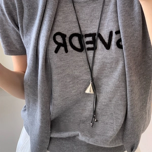 Detail of silver triangular metal pendant on black cord over grey knitted sweater