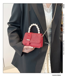 Close-up of red mini square bag with pearl handle and golden chain on model