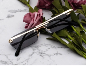 Detailed view of rimless rectangle sunglasses with dark grey lenses and gold metal frame