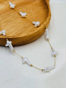 Macro detail of golden chain necklace featuring white cross-shaped baroque pearls on silk