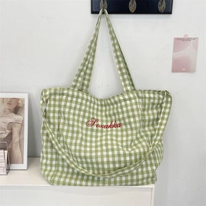 Detailed view of green plaid canvas tote bag featuring red Pozakka embroidered lettering