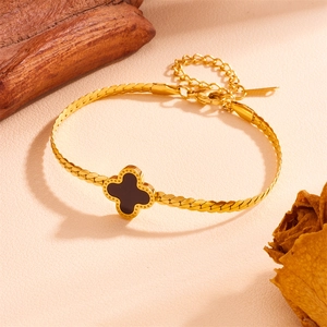 Detail of gold curb chain necklace featuring black clover charm on rustic wood background