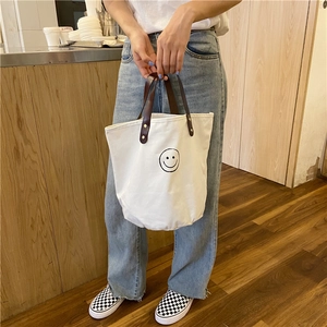 Close-up of white canvas tote bag featuring black line drawing smiley face and leather handle