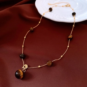 Detailed macro shot of vintage tiger eye stone pendant and golden beaded necklace chain