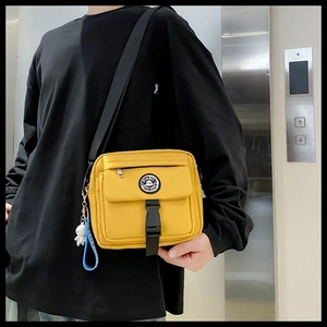 Detail of yellow nylon messenger bag featuring blue astronaut keychain and adjustable strap