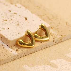 Close-up of heart-shaped gold earrings on a textured stone display with soft lighting