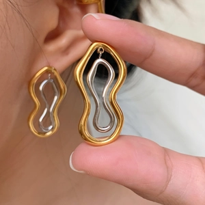 Macro detail of two-tone wave earrings in gold and silver showing on-ear wearing effect