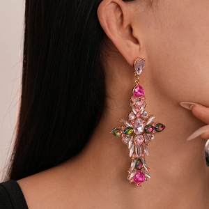 Close-up of vintage baroque cross earrings featuring pink and green crystals on a gold base