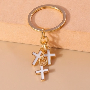 Macro detail of three white enamel cross charms on a golden flat metal key ring