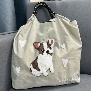 Beige nylon tote bag with French Bulldog embroidery and woven rope handles on a sofa