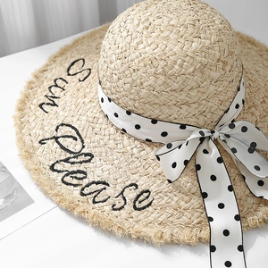Detail of raffia sun hat featuring frayed edges and 'Sun Please' black embroidery