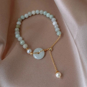 Detail of jade bead bracelet with pearl charm and gold clasp on silk background