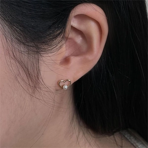 Close-up of a heart-shaped gold earring with a white pearl on a model's ear